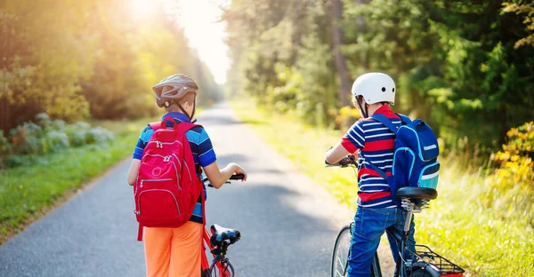 Niños con mochilas en bicicleta en el parque cerca de la escuela — Foto de Stock