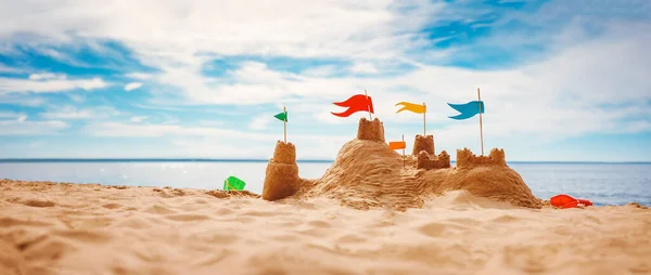 Piaszczysty zamek z kolorowymi flagami na plaży morza — Zdjęcie stockowe