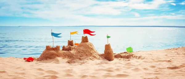 Castillo de arena con banderas de colores en la playa del mar — Foto de Stock