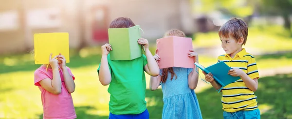 Crianças de pé no parque coberto de rostos com livros. — Fotografia de Stock