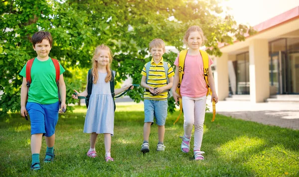 Lindos niños con mochilas caminando en el parque cerca de la escuela —  Fotos de Stock