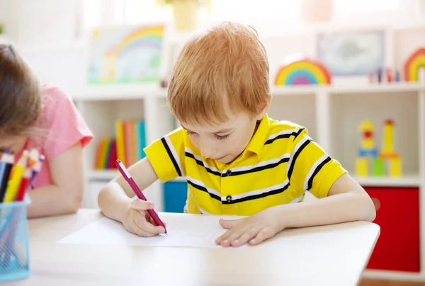 Iskolásfiú az osztályteremben ül az asztalnál és leckét ír.. — Stock Fotó