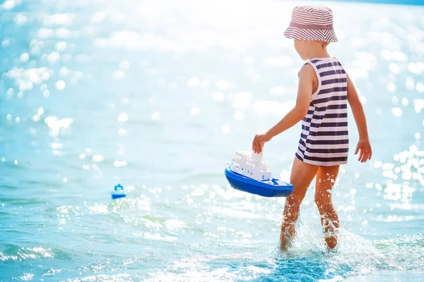 Little boy playing on the sea beach with toy ship — Stockfoto