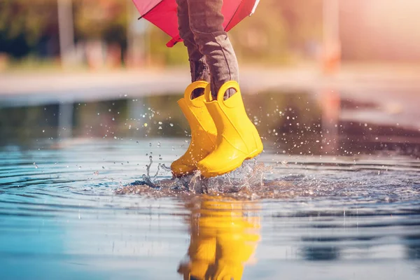 Child jumping in the puddle in yellow rubber boots. Concept of childhood.