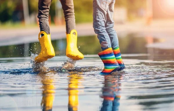 Children jumping in the puddle in rubber boots. Concept of childhood and friendship.