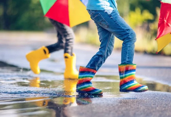 Children jumping in the puddle in rubber boots. Concept of childhood and friendship.
