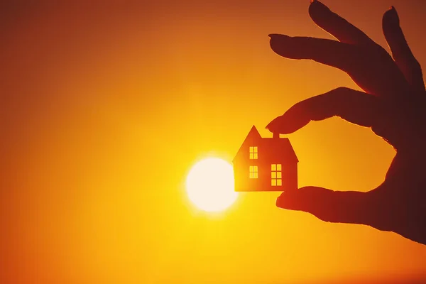 Womans hand holding a model of a house on sunset evening. Concept of buying or selling a new appartment.