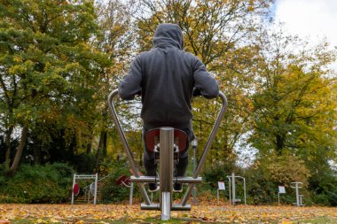Sonbaharda kürek çekme makinesinde egzersiz yapan genç bir adam. Arkadan görüntüle.