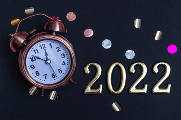 Alarm clock with gold numbers on a black background. Minimal concept of the new year 2022. close-up