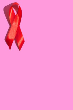 Uluslararası AIDS Günü. Pembe arka planda sert gölgeli kırmızı kurdele. AIDS farkındalığı konsepti. Dikey fotoğraf