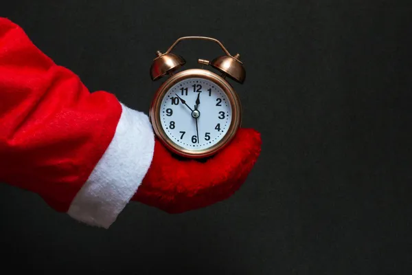 Şenlik konsepti. Noel Baba 'nın elinde siyah bir arka planda bakır rengi çalar saat var.
