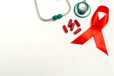 Dünya AIDS Günü Aralık ayı için tıbbi konsept. Kırmızı kurdele, yeşil tıbbi steteskop ve beyaz arka planda kırmızı terapi hapları veya vitaminler. Kopyalama alanını kapat