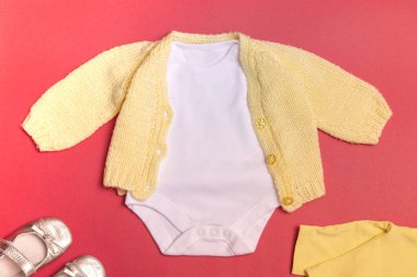 Renkli bir arka planda, örülmüş sarı ceketli ve sarı tozluklu boş beyaz bir bebek tulumu yeni doğan kıyafetlerinin bir maketi. Kopyalama alanı ile