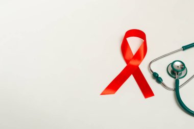 Dünya AIDS Günü Aralık ayı için tıbbi konsept. Kırmızı kurdele, beyaz arka planda yeşil tıbbi steteskop. Kopyalama alanını kapat