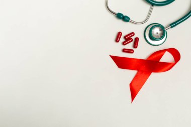 Dünya AIDS Günü Aralık ayı için tıbbi konsept. Kırmızı kurdele, yeşil tıbbi steteskop ve beyaz arka planda kırmızı terapi hapları veya vitaminler. Kapat.
