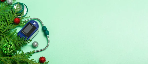Tıbbi konsept: Noel 'i sağlık hizmetlerinde kutlamak. Düz bir steteskopun üst görüntüsü, nabız oksimetresi, yeşil arkaplanda köknar dalları. Kopyalama alanı olan. Pankart