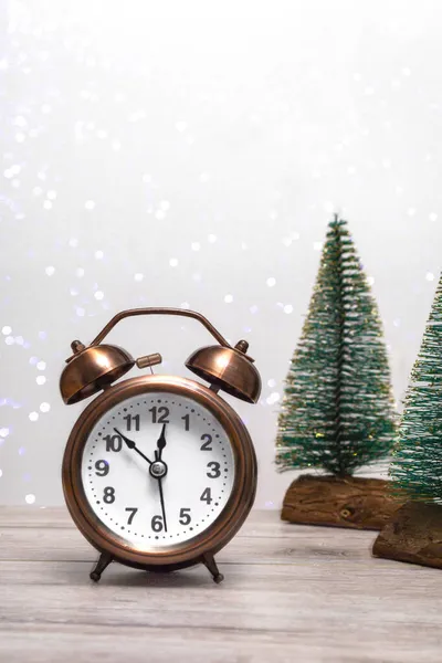Noel arka planında küçük Noel ağaçları ve arka planda ışıklarla birlikte eski bir çalar saat var. Noel temasını kapat. Dikey fotoğraf