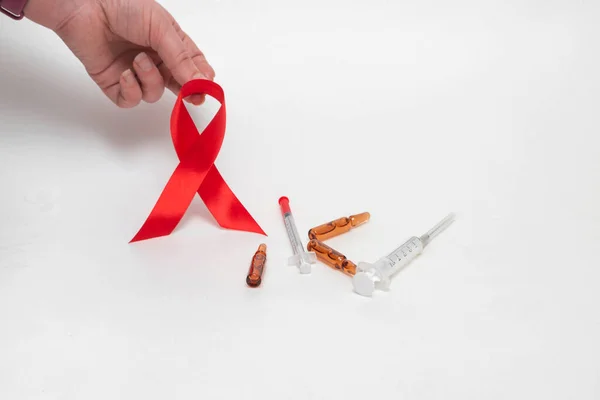 Orvosi koncepció az AIDS világnapjára decemberben. Piros AIDS tudatosság szalag kapaszkodott egy nő kezét egy fehér háttér. Közelről. — Stock Fotó