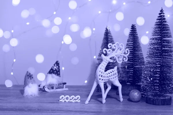 Noel ve Yeni Yıl dekoru. Noel geyiği, 2022 numara, kızaktaki cüce ve Noel ışıkları olan çok peri arkaplanındaki Noel ağaçları. Noel kartı kapanıyor. Tek Renkli