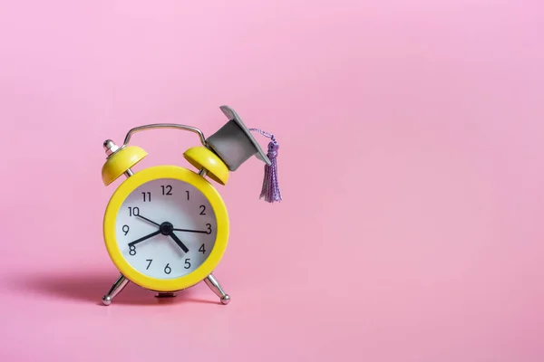 Gul väckarklocka med examen mössa på rosa bakgrund närbild med kopia utrymme — Stockfoto