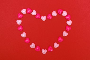 Kırmızı arka planda küçük kalplerden yapılmış kalp şeklinde bir çerçeve. Sevgililer Günün kutlu olsun, Anneler Günü. Kartpostal ya da yaratıcı tasarım kavramı. Yukarıdan görüntüle.