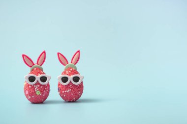 Mavi arka planda tavşan kulaklı ve güneş gözlüklü renkli Paskalya yumurtası. Satış afişi, model şablonu. Kopyalama alanı ile