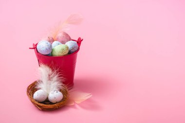Pembe arka planda bir Paskalya kompozisyonu, bir kova ve yumurtalı bir yuva fotokopi alanına yakın.
