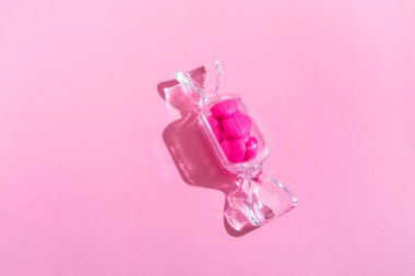 Şeffaf şeker şeklindeki kutuda tatlı kalp lolipopları ve pembe arka planda sert gölgeli fotokopi alanı var. Sevgililer Günü konsepti, Anneler Günü. Pankart