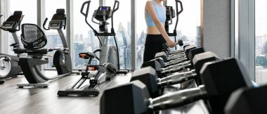 Spor kıyafetleri giyen, spor salonunda spor yaparken elinde dambıl tutan bir kadın.