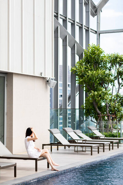 A beautiful young girl in white sitting on a summer terrace by the pool