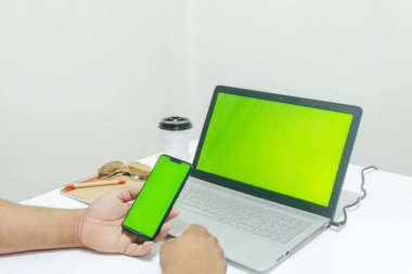 Bilgisayarda çalışırken cep telefonunu kontrol eden kişi