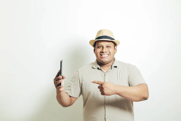 Şapkalı İspanyol adam, beyaz arka planda çok mutlu bir şekilde cep telefonunu işaret ediyor.
