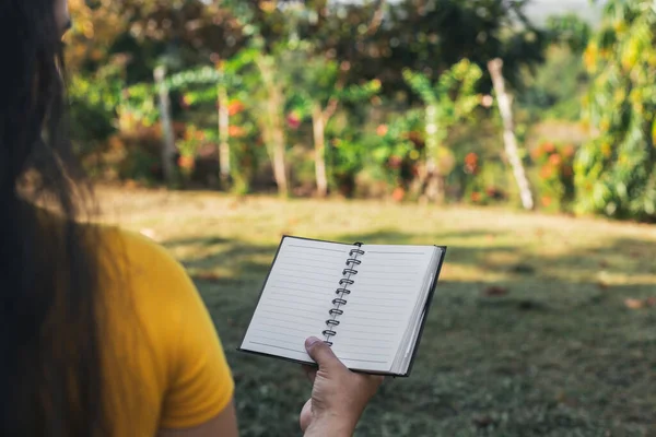 Latin bir kadın sahada oturmuş defterini okuyor. Elinde defter tutan bir kadın.