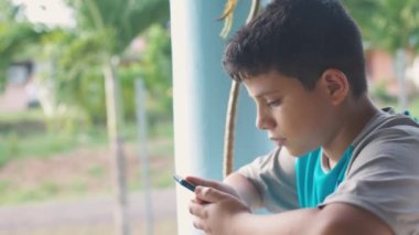 boy in the doorway looking at the mobile screen, leaning against iron fences.