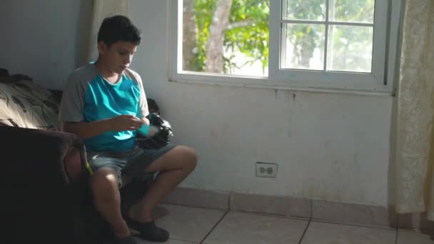 Boy playing with a glove and a baseball, sitting in the living room of the house. — Vídeo de Stock