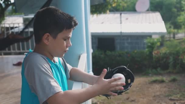 男孩拿着手套和棒球玩耍，靠着白色的栅栏 — 图库视频影像