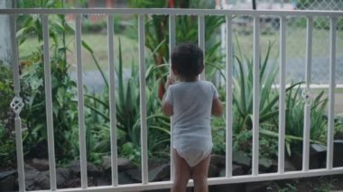 baby playing on the railing, pointing at objects with his finger