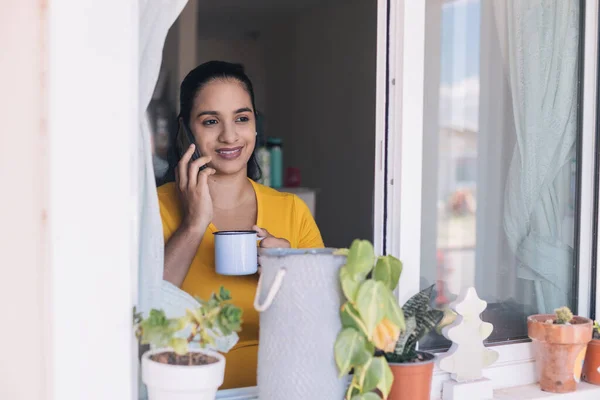 Kadın pencerenin kenarında telefonla konuşuyor.