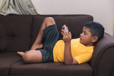 Çocuk çikolata sandalyesinde uzanıp cep telefonuna bakıyor.