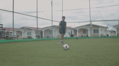 Latin çocuk futbol sahasında antrenman yapıyor, kaleye şut atıyor..
