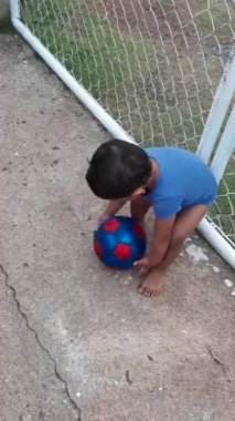 Mavi elbiseli Latin bebek mavi futbol topuyla oynuyor.