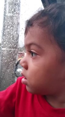 Yağmur yağarken pencereden dışarı bakan Latin bebek.