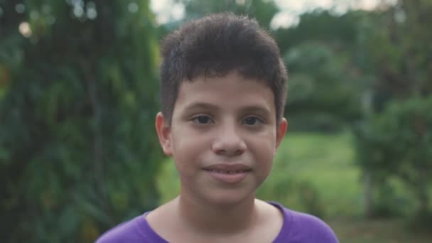 Chico Latino Mirando Cámara Con Suéter Púrpura Campo Verde Plano — Vídeos de Stock