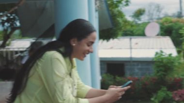 Latin kadın cep telefonunda yazarken gülümsüyor, beyaz parmaklıklara yaslanıyor, orta ölçekli..