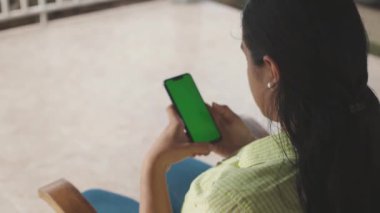 Tanımlanamayan Latin bir kadın yeşil ekranlı, dikey cep telefonuna bakıyor..