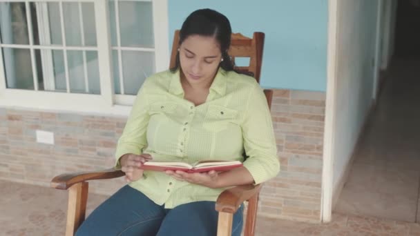 Mulher Latina Com Livro Vermelho Leitura Sentada Uma Cadeira Balanço — Vídeo de Stock