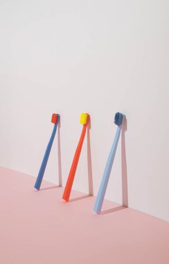 Pastel pembe arka planda üç renkli diş fırçası olan modaya uygun minimal kompozisyon. Modern estetik.
