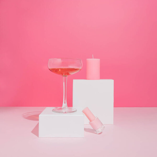 Girly pastel pink set with nail polish, romantic candle and rose wine glass. Modern self care aesthetic.