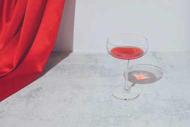 Şarap partisi kadehiyle romantik kırmızı kompozisyon ve mermer arka planda kırmızı saten perde. Modern minimal estetik.