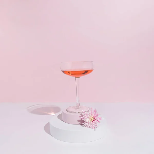Minimal pastel party concept with bright pink flower and wine glass. Modern spring or summer aesthetic.